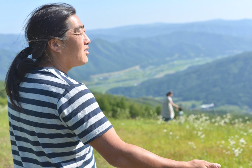山谷川のパラグライダーの丘に立つ伊勢崎さんと、遠くで遊ぶまゆみさんと歩くん